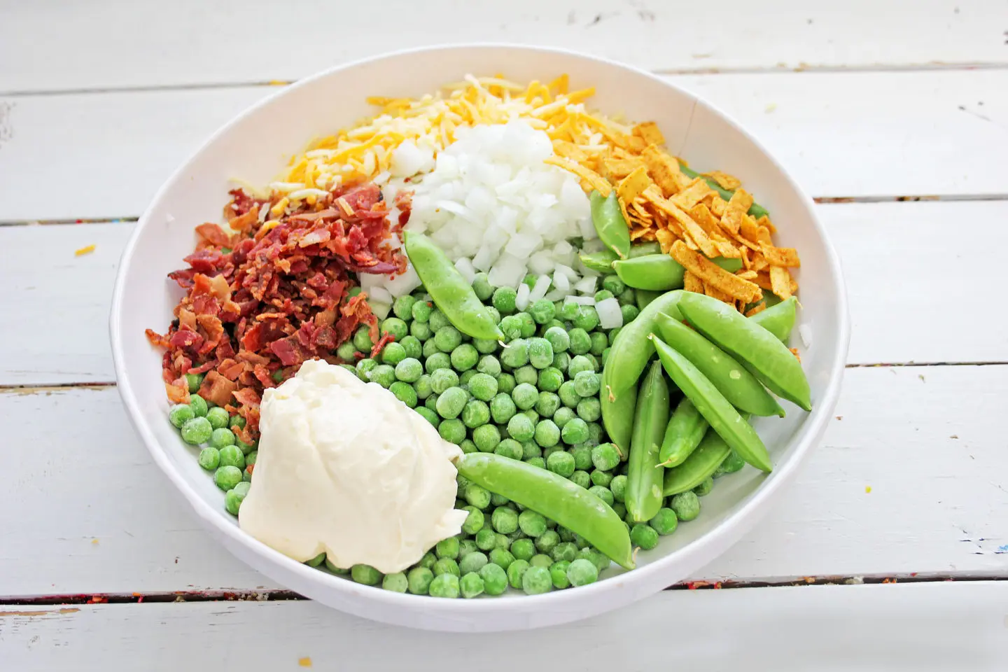 Ingredients for green pea salad recipe. Bacon, sweet peas, cheddar cheese, onion, sour cream.