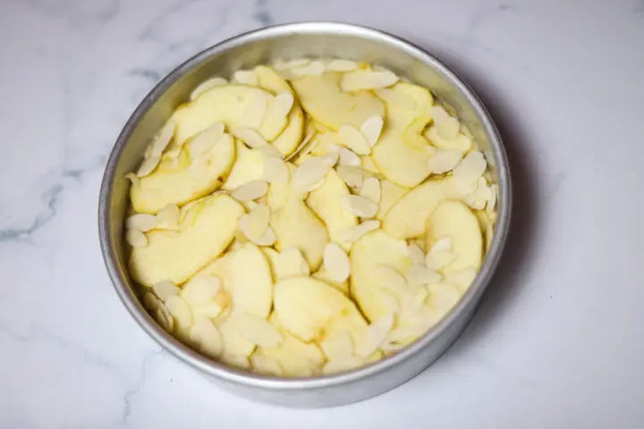 Apple cake in a pan topped with sliced apples and almonds.