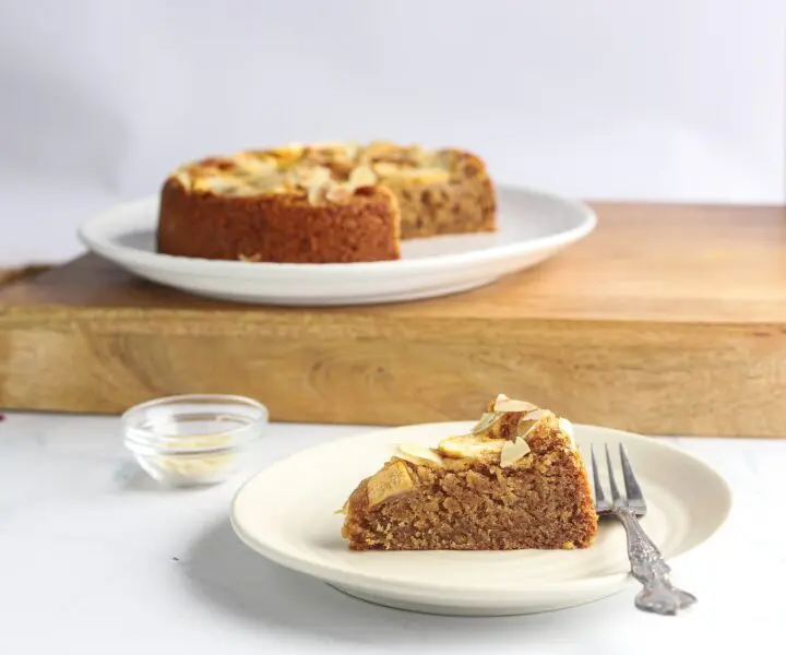 A plate with a slice of almond cake with apples and almonds.