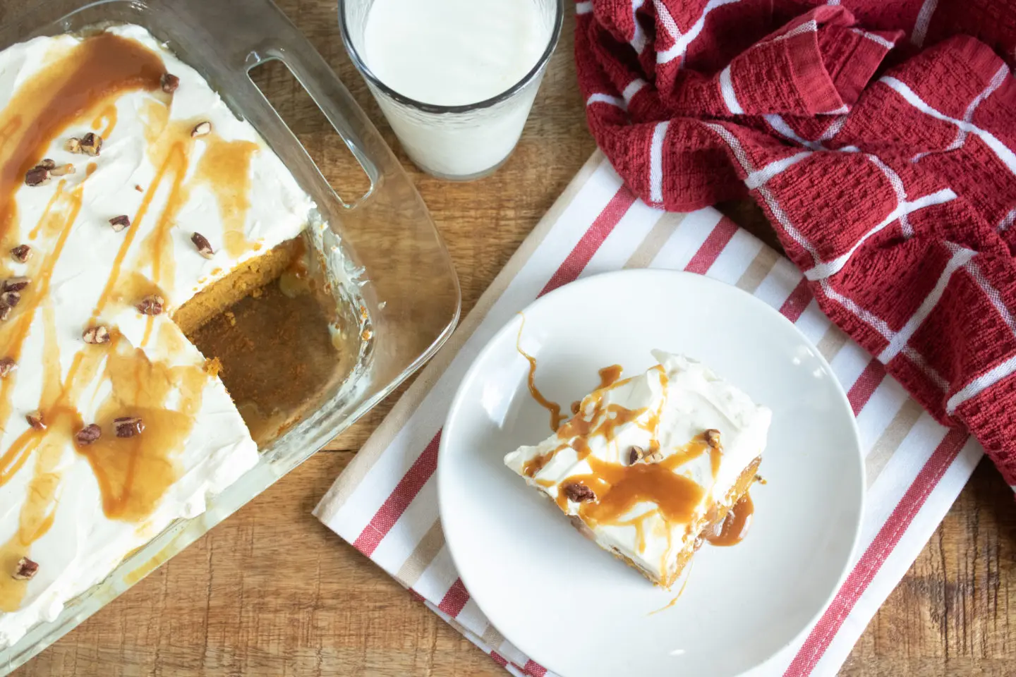 A piece of pumpkin poke cake on a plate with a glass of milk.