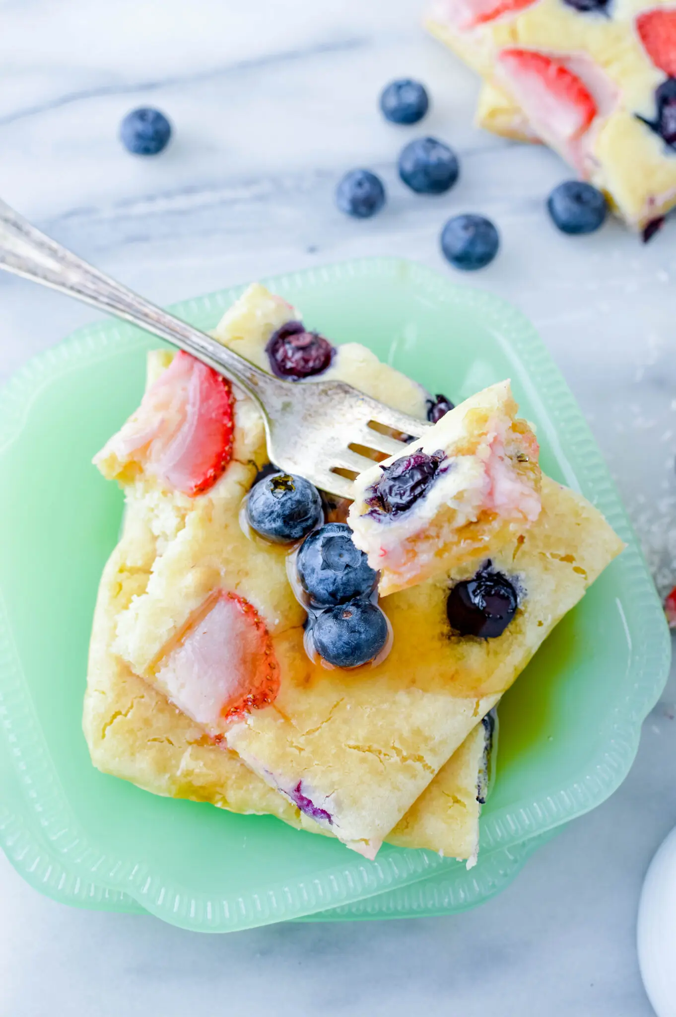 a plate of sheet pan pancakes with fruit and syrup on top.