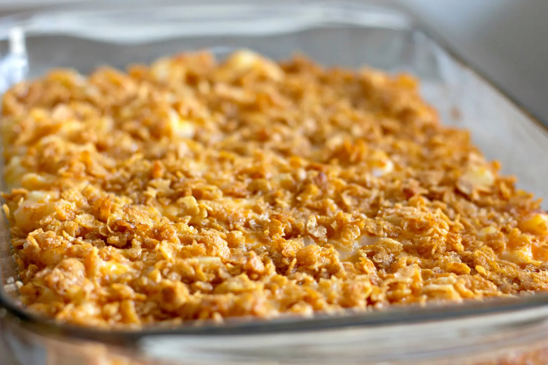 A pan of cheesy potatoes topped with buttered, crushed cornflakes.