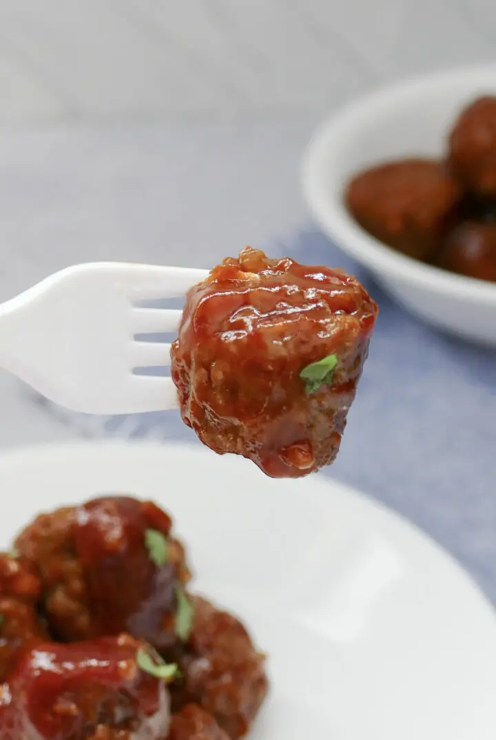 A fork with a crockpot meatball covered in sweet and spicy sauce.