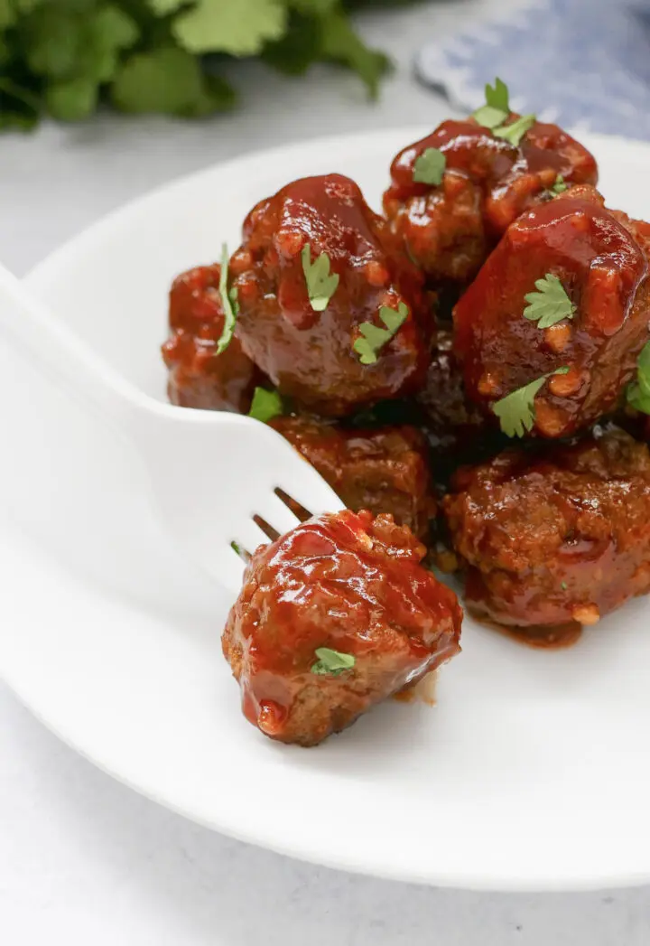 A plate of crockpot meatballs with a fork about to take one. 