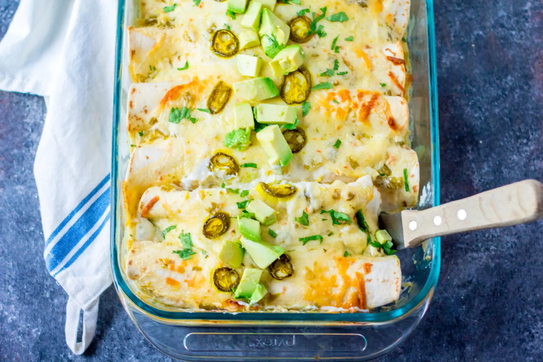 a pan full of chicken enchiladas with white sauce and sliced jalapenos on top.