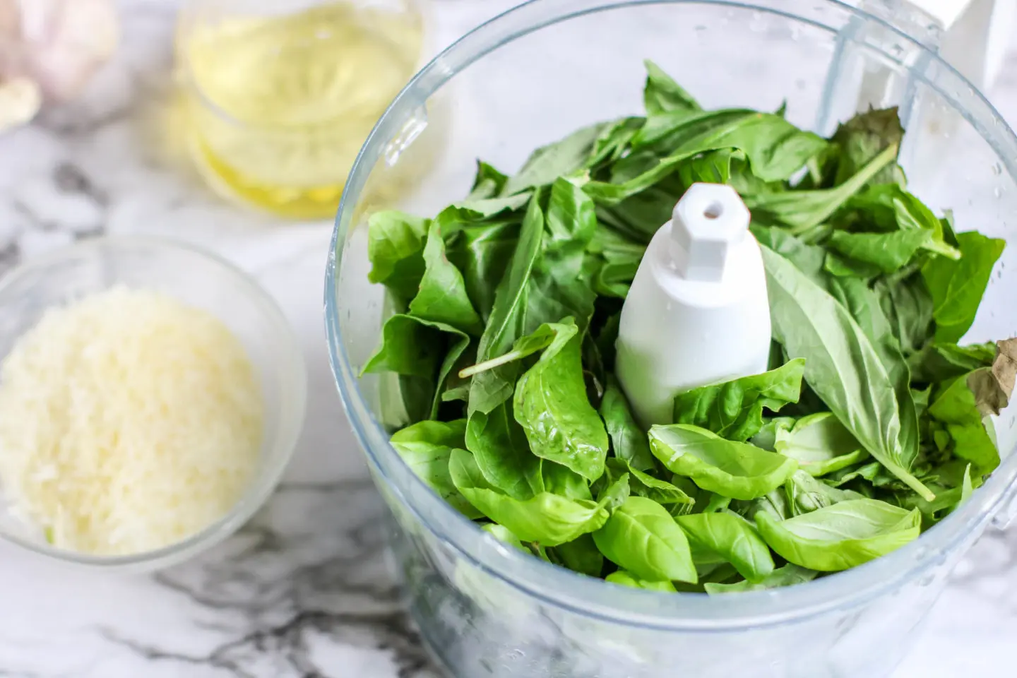 Fresh basil in the food processor with parmesan cheese and oil getting ready to go in to make a pesto.