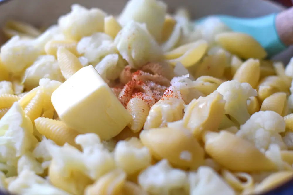 butter and spices being added to cauliflower macaroni and cheese