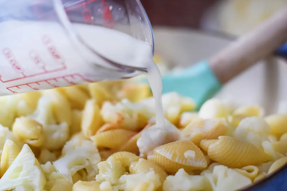 milk being poured into cauliflower macaroni and cheese