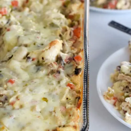 A pan of cheesy chicken and rice hotdish with 2 plates of it nearby.