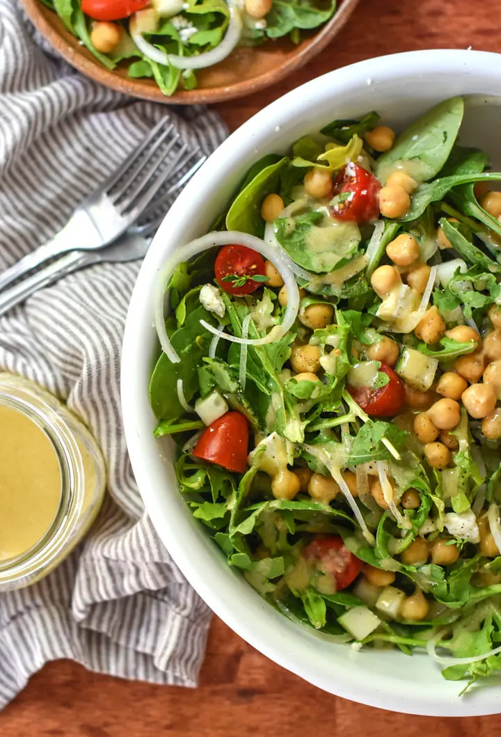 A bowl of arugula mixed with chickpea and fresh veggies for the ultimate summer salad!
