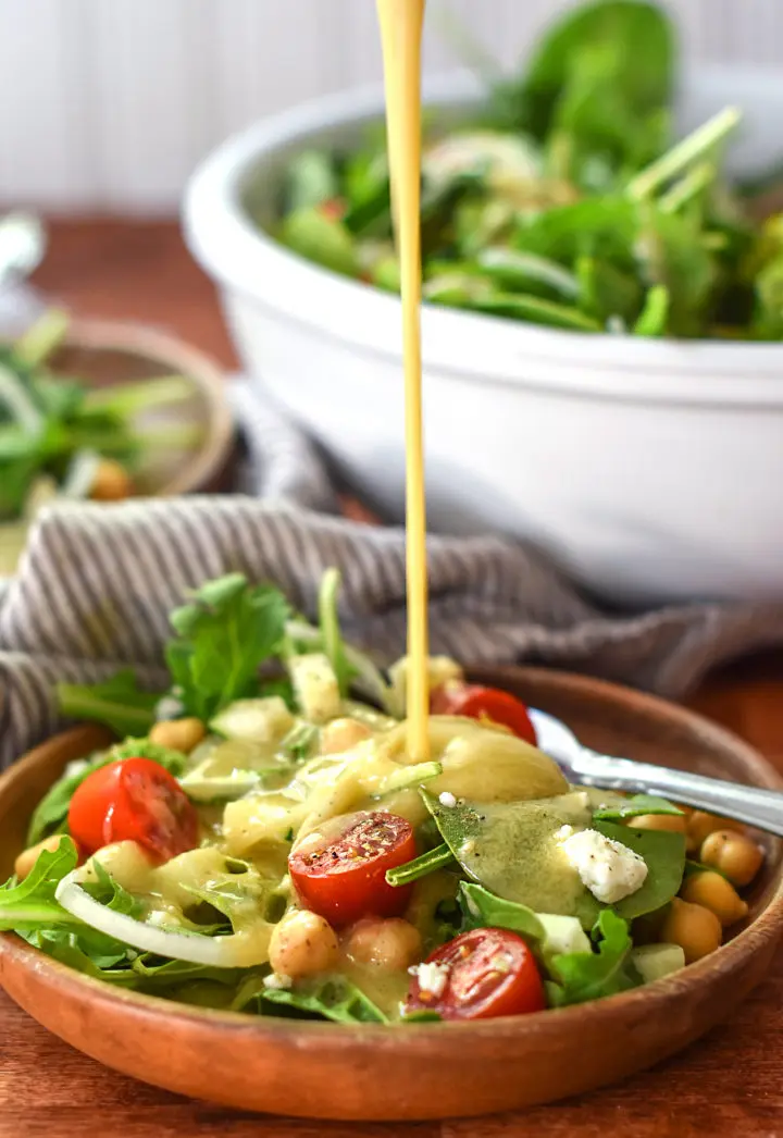 Creamy tahini dressing poured over a beautiful chickpea and arugula salad