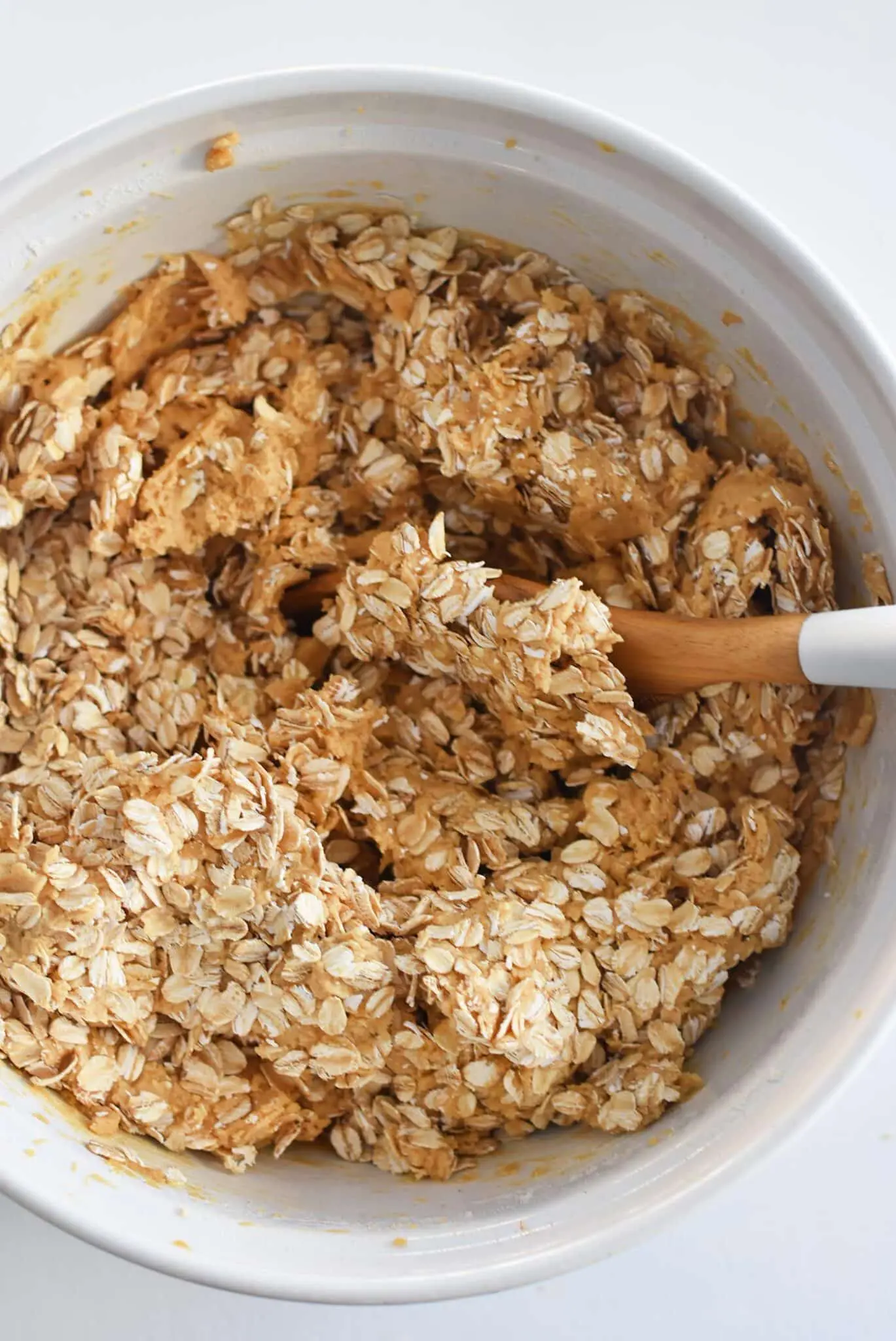 A wooden spoon stirring oatmeal into a bowl of peanut butter batter.