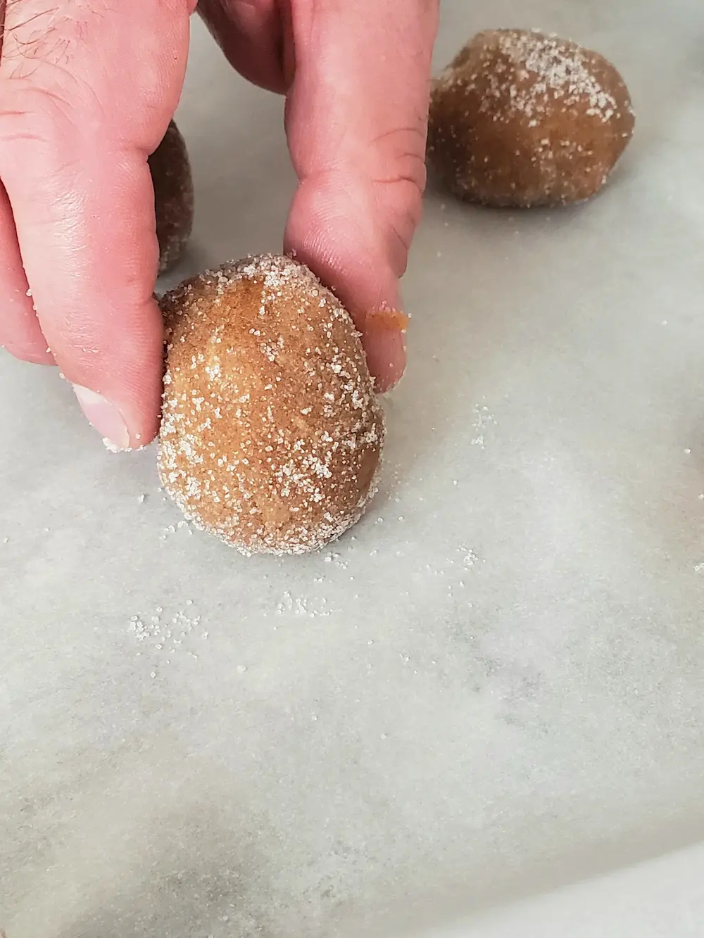 A ball of peanut butter cookie dough rolled in sugar being placed on parchment paper for baking.