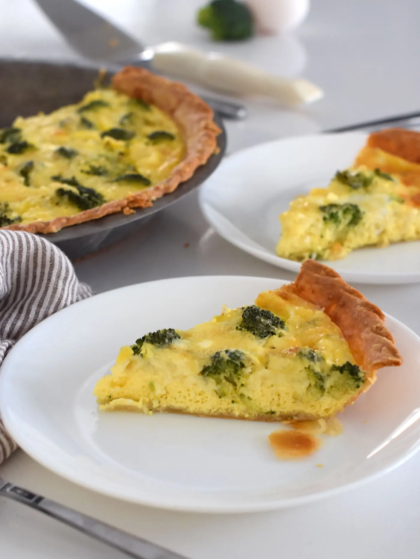 broccoli and cheese quiche on 2 plates in a pie pan.