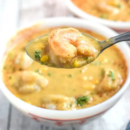 A bowl of shrimp and corn chowder with a bit on a spoon