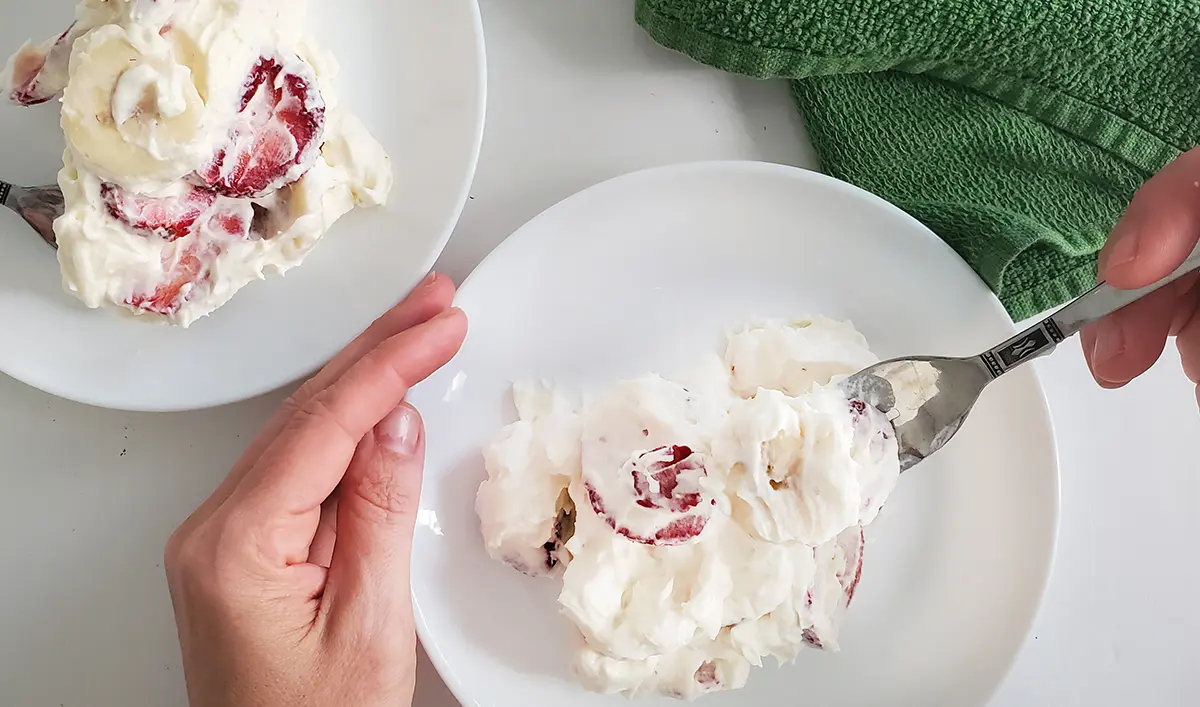 a plate of strawberry cheesecake salad with a hand holding a fork