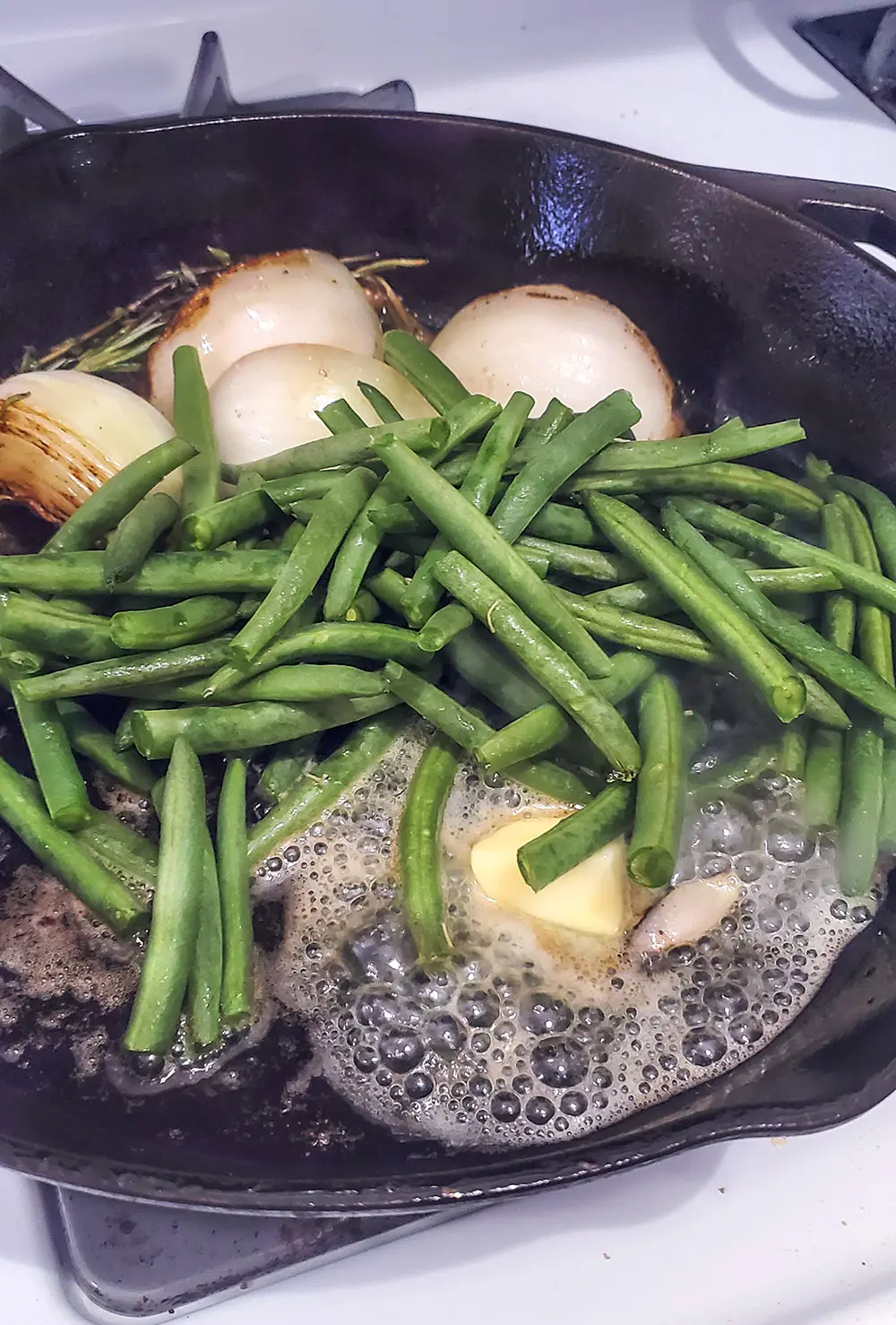 Green beans in a cast iron pan with butter and onions