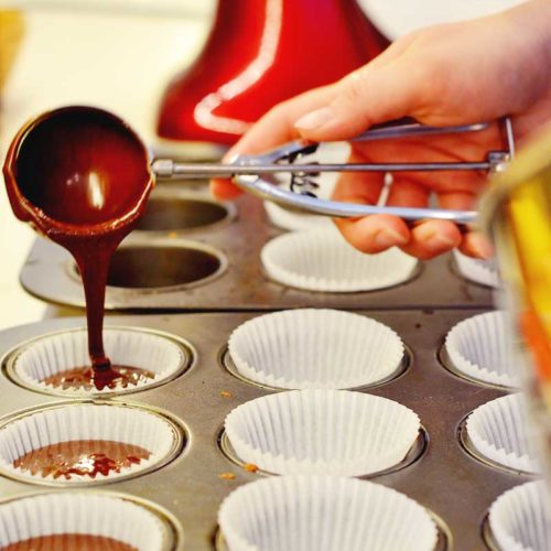 scooping batter into a c cupcake pan with liners in it.