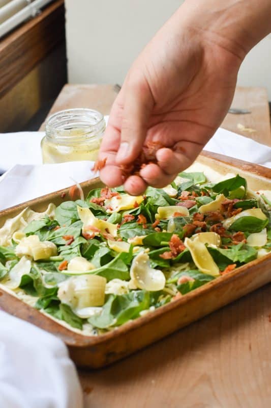 toppings being put on a garlic white pizza