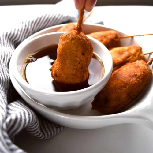 breakfast corn dogs being dipped into maple syrup