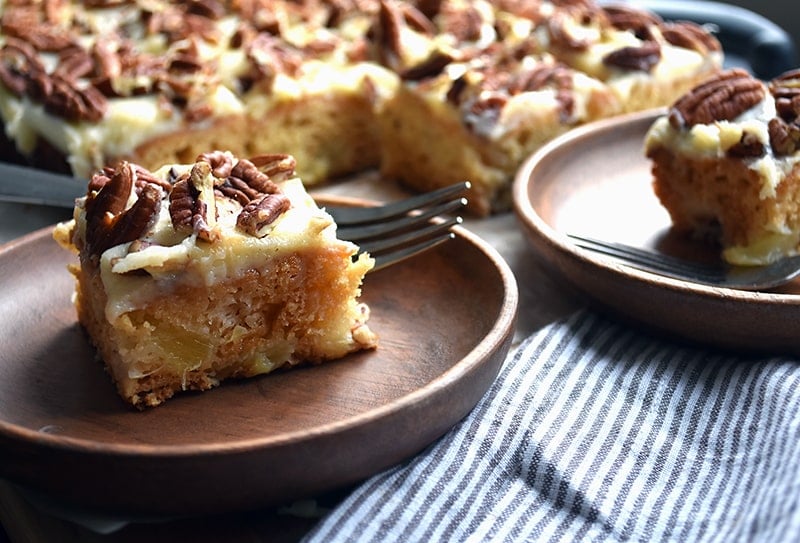 a slice of perfectly moist pineapple cake with cream cheese frosting and pecans on top.