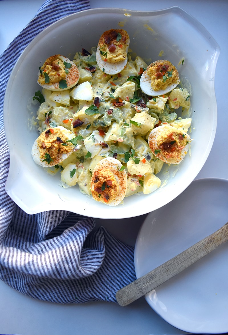 deviled eggs on top of potato salad in a bowl with a plate and fork next to it.