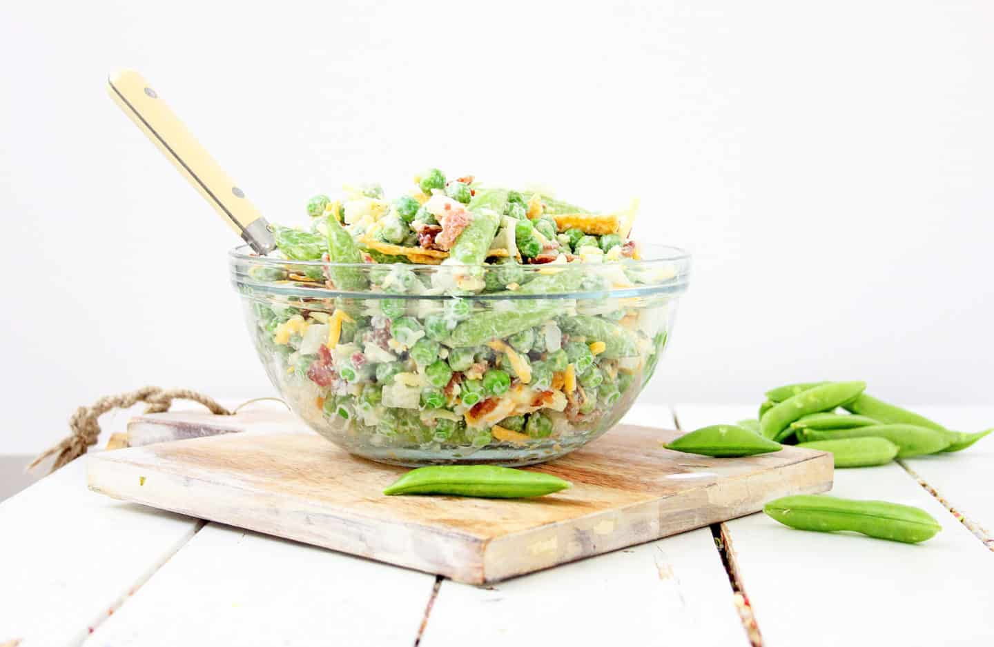 A bowl of green pea salad with fresh peas, bacon, shredded cheese, and more.