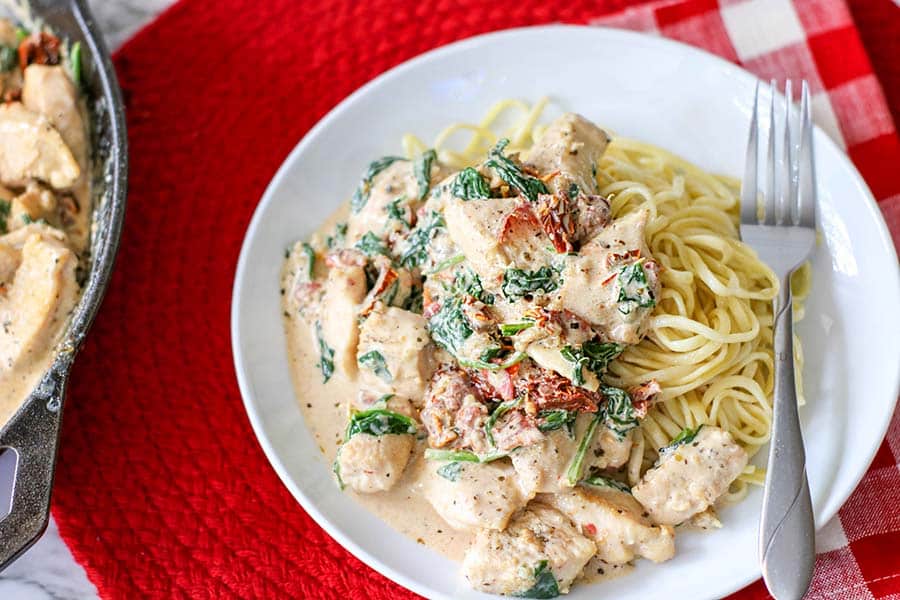 Creamy Tuscan Chicken with sundried tomatoes, spinach, and served over pasta.