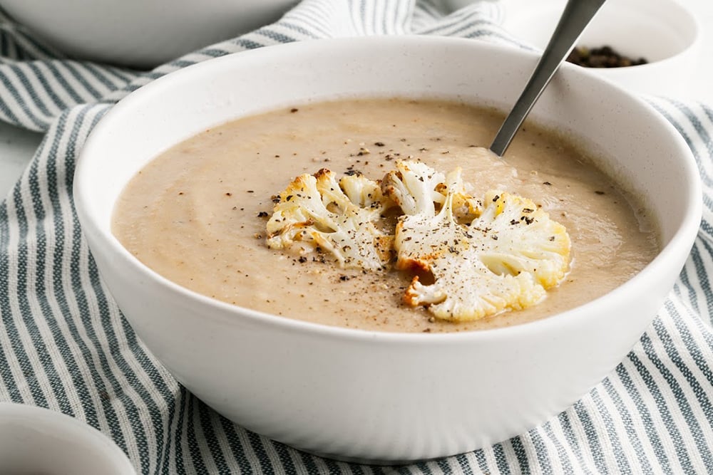 Creamy bowl of cauliflower soup with roasted fresh cauliflower on top.