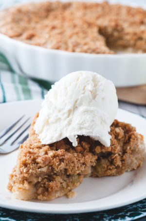 rhubarb pie on a plate with ice cream on it. A pie is in the background.