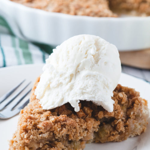 rhubarb pie on a plate with ice cream on it. A pie is in the background.