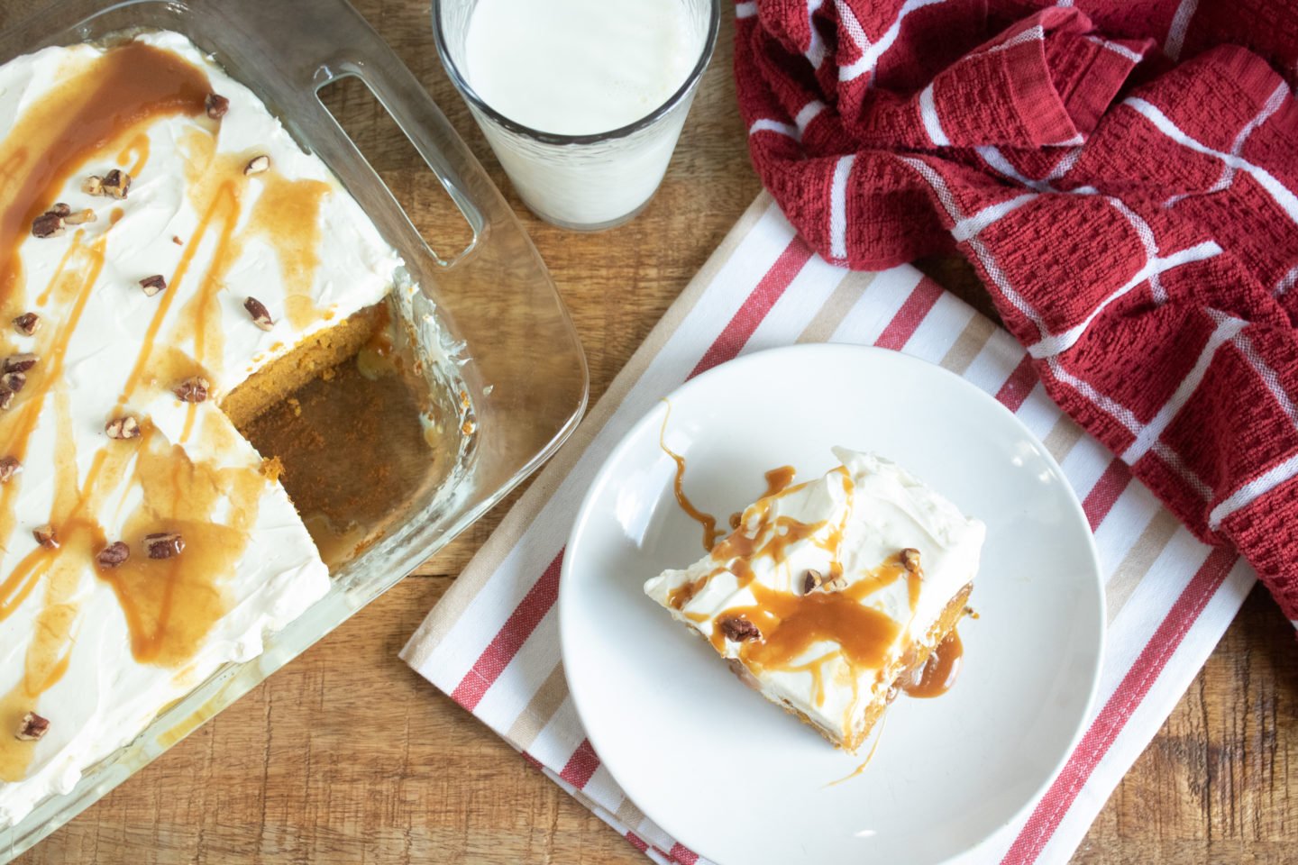 A piece of pumpkin poke cake on a plate with a glass of milk.