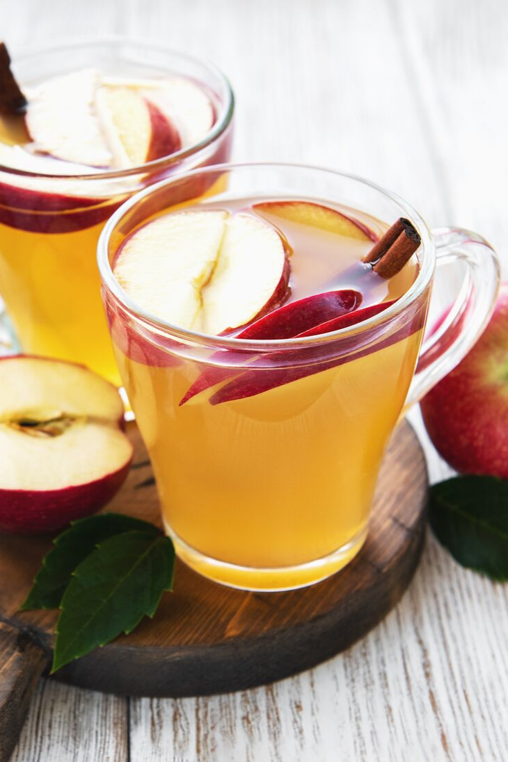 Apples, cinnamon, and whiskey in a clear mug filled with a hot toddy.