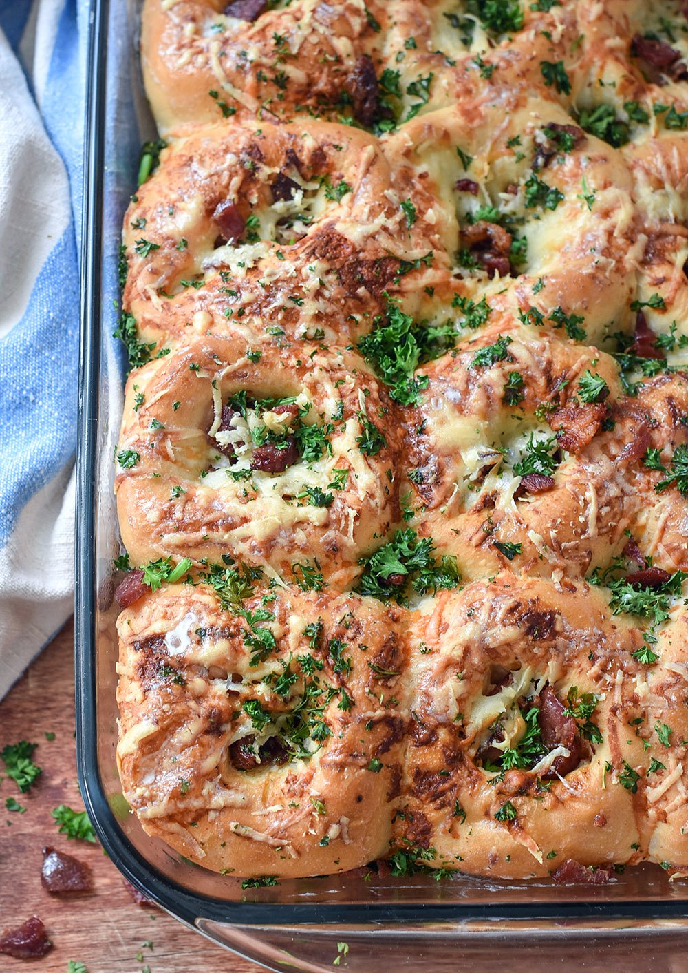 Baked dinner rolls with cheese, bacon, and fresh parsley on top.