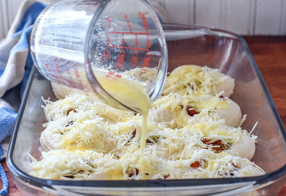 A pan of dinner rolls with cheese and bacon getting melted butter poured over.