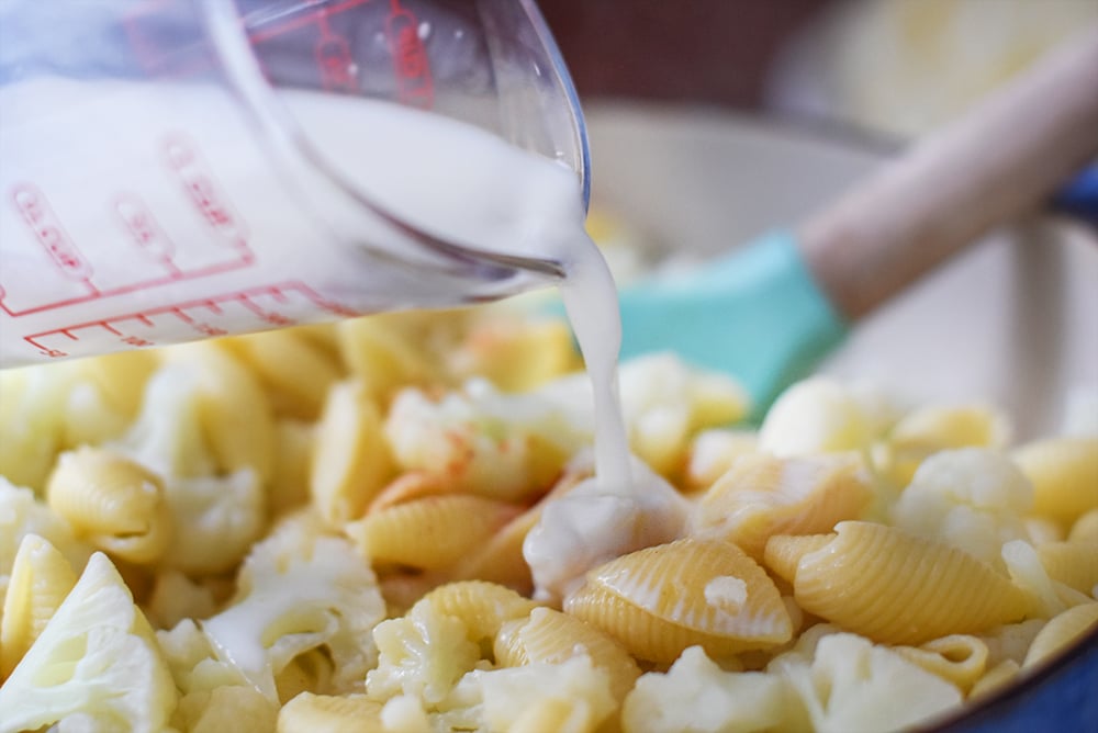 milk being poured into cauliflower macaroni and cheese