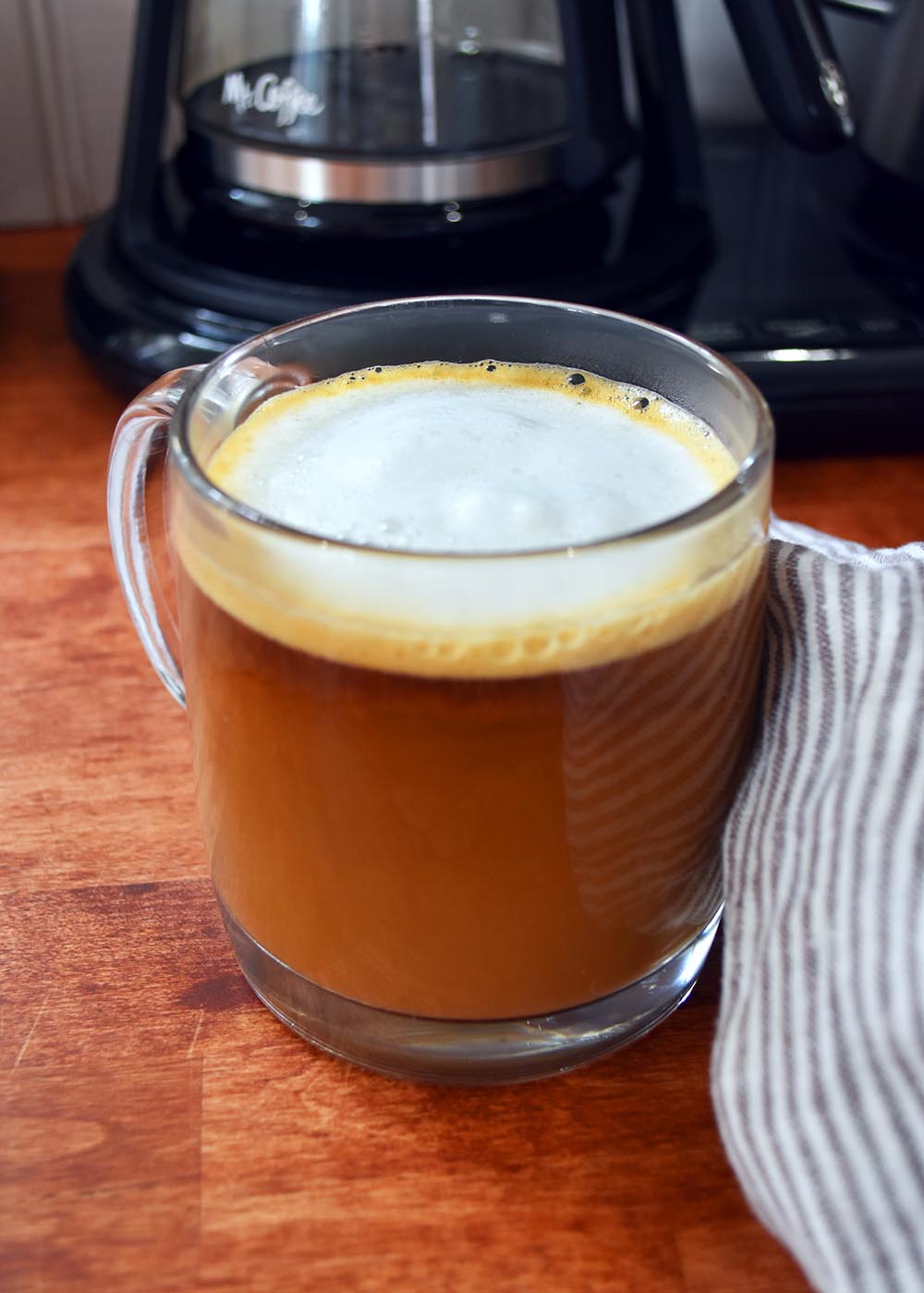 Delicious coffee with frothed milk on top and a Mr. Coffee in the background.