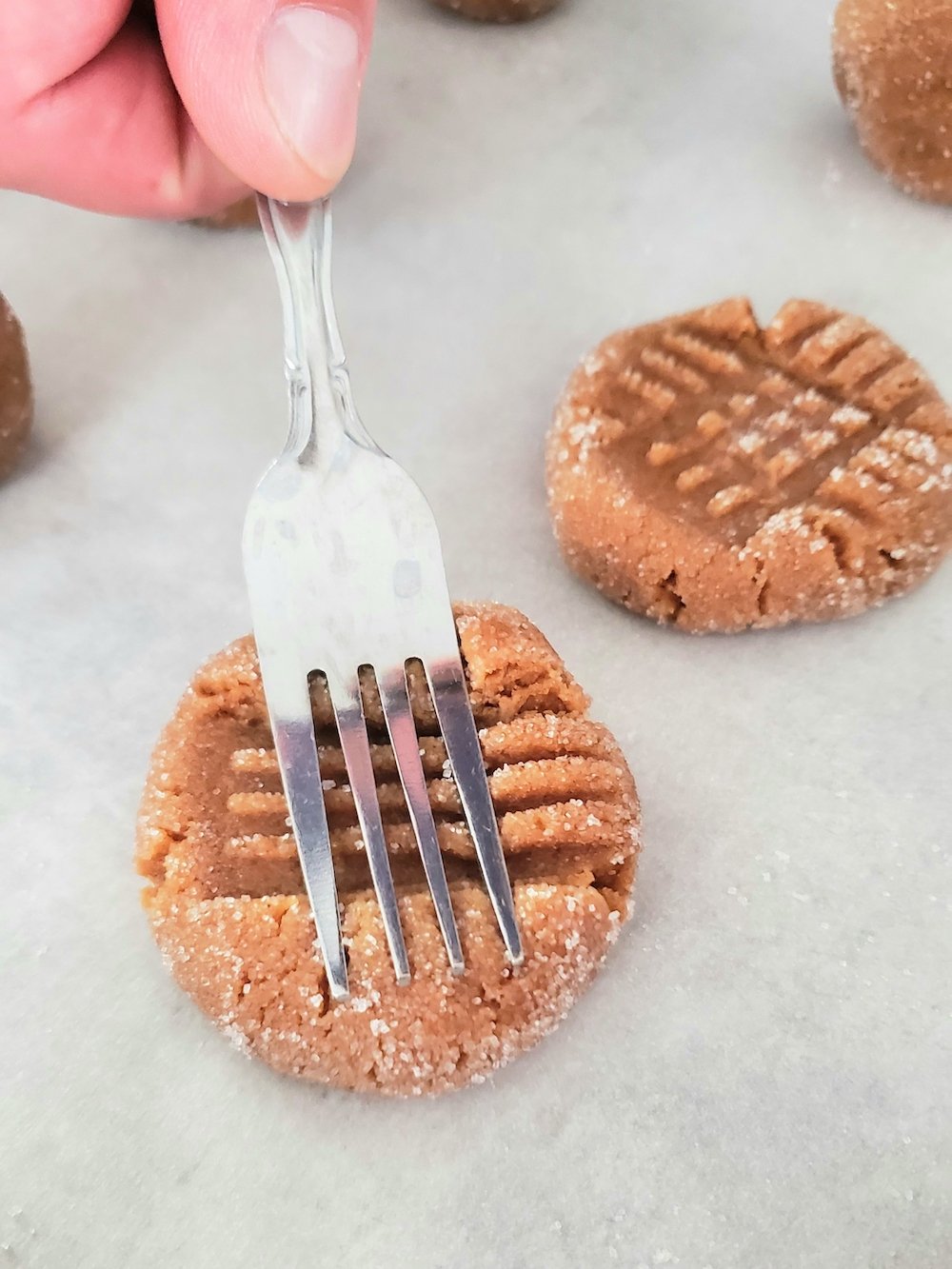 Pressing a fork into perfect 3 ingredient cookies with a bit of sugar dusted on top.