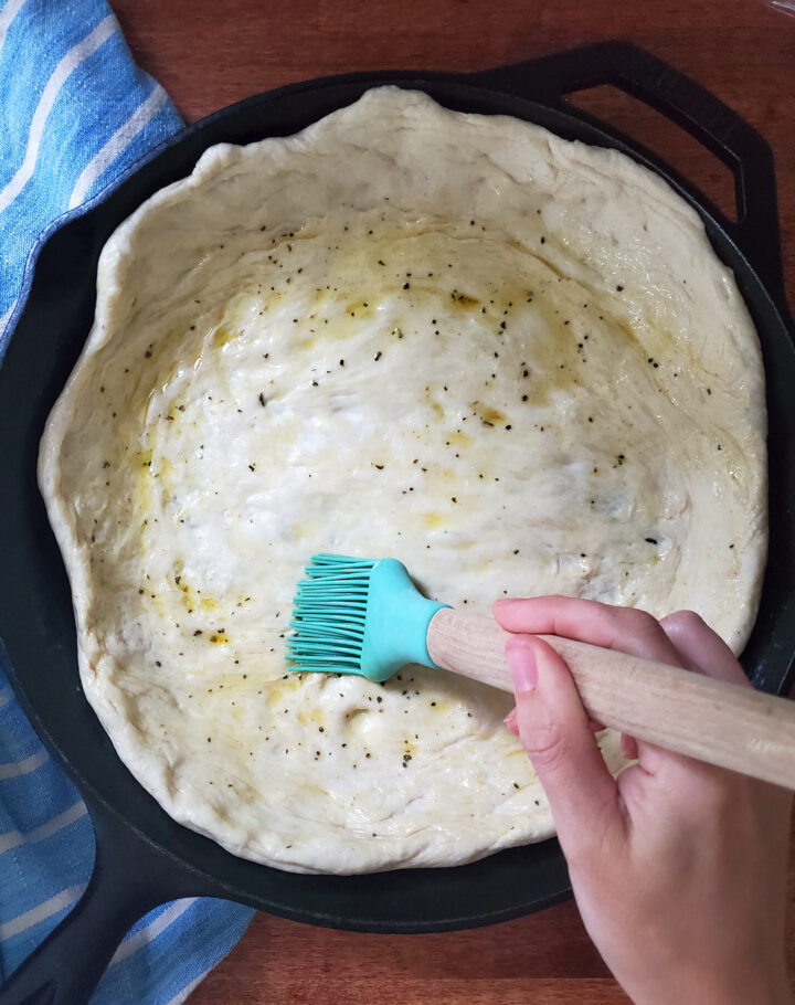 brushing a deep dish pizza crust with seasoned olive oil