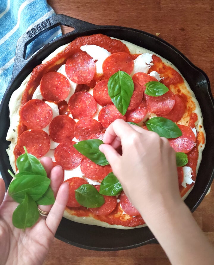 deep dish pizza in a cast iron pan being topped with fresh basil