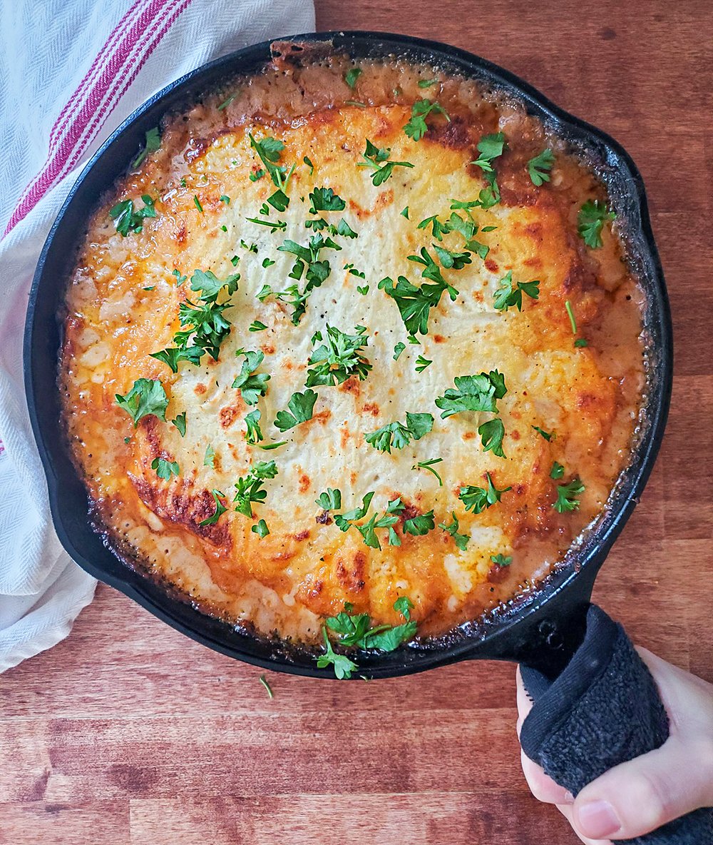 A cast iron shepherd's pie with cheese and topped with fresh parsley.