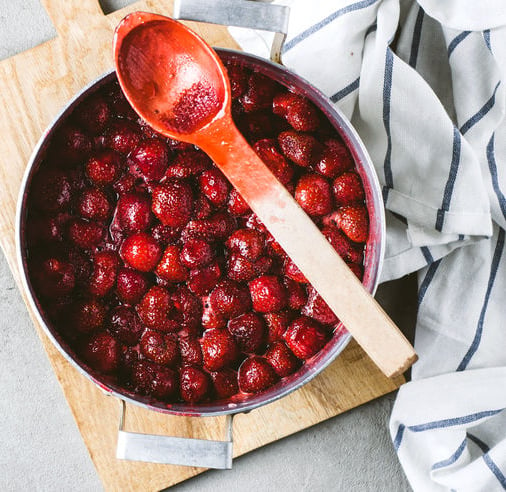 Homemade strawberry jam in an alluminium pan on a grey concrete background