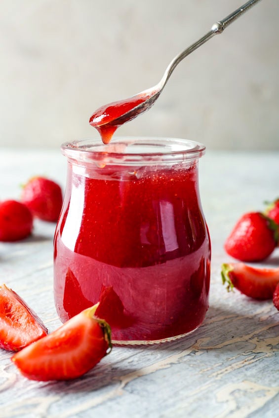 Glass jar and spoon with strawberry jam on wooden table